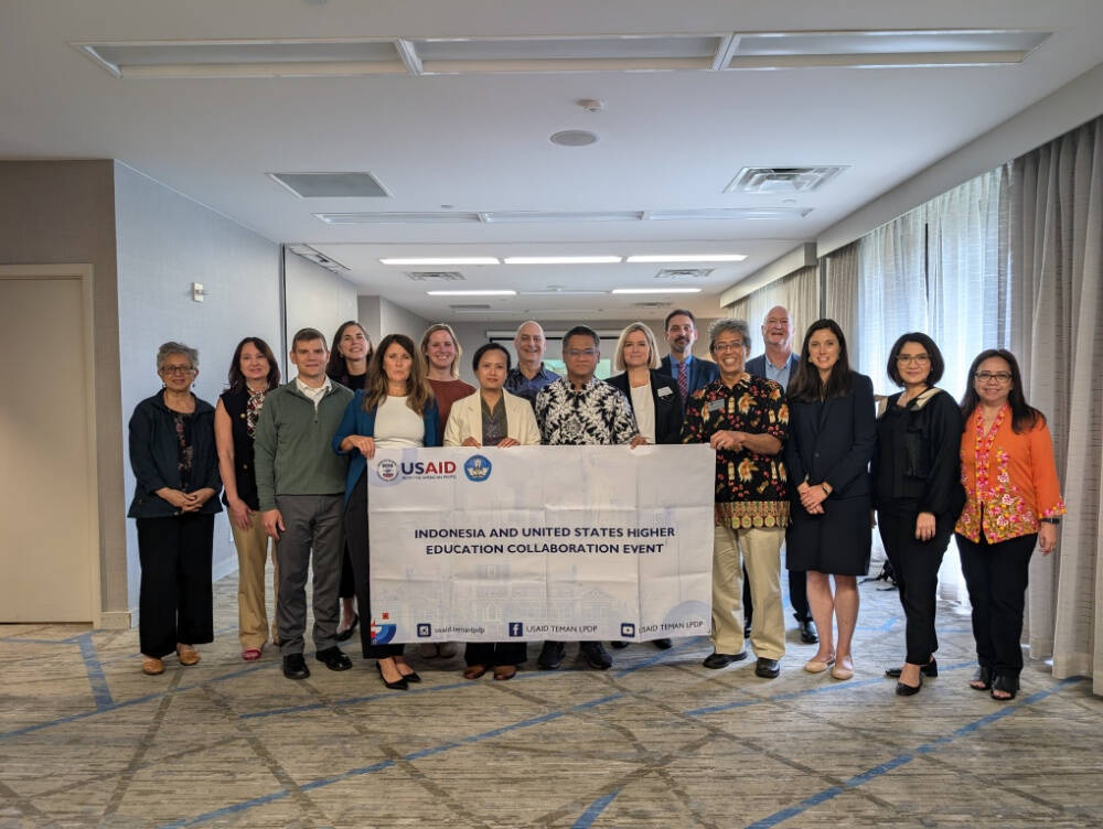 A group of people stands together in a conference room holding a banner that reads "Indonesia and United States Higher Education Collaboration Event," with USAID and other partner logos.